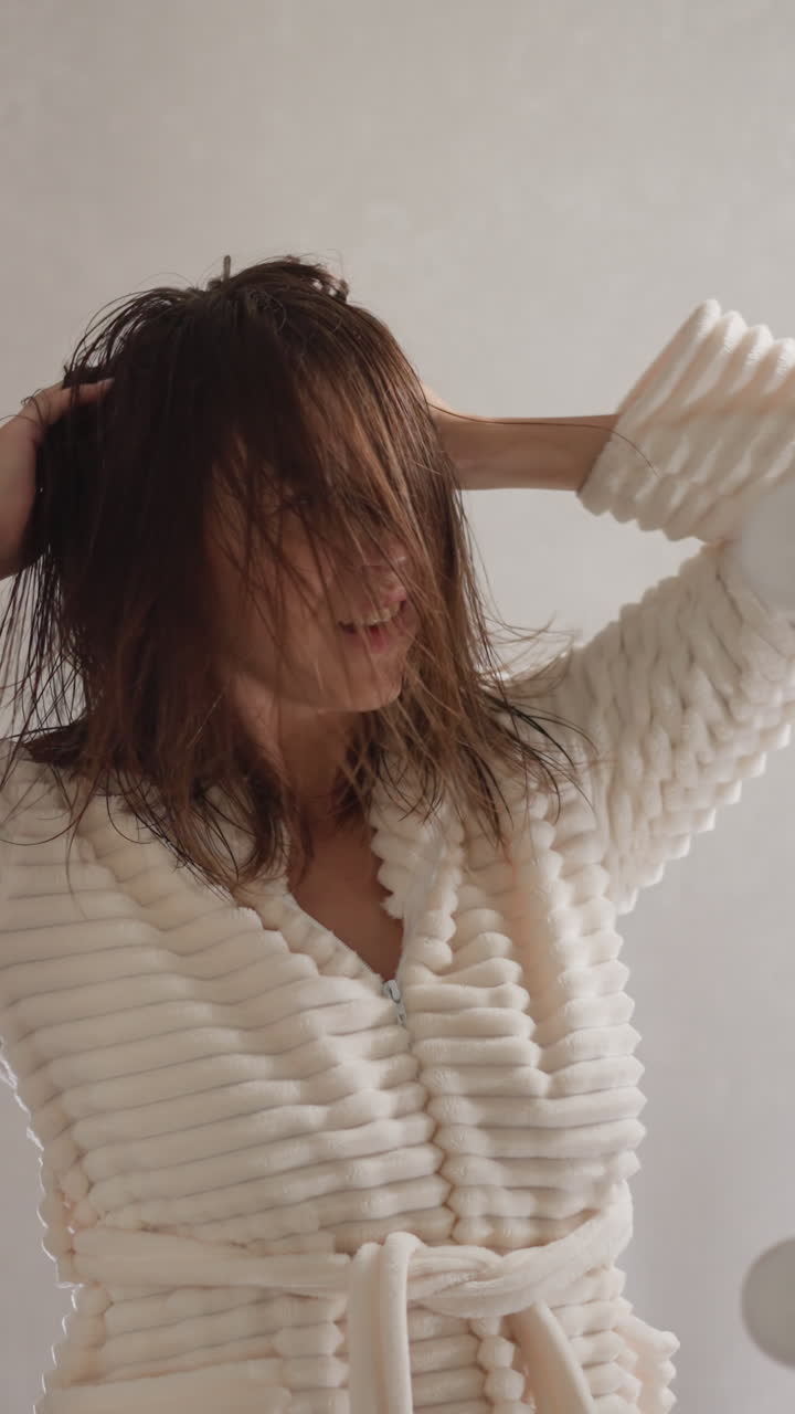 여성은 화장실에서 헤어드라이어 없이 은 머리카락을 건조시니다. 매력적인 갈색 여성은 샤워를 한 후 은머리를 곧게하는 음악을 듣고 있습니다.