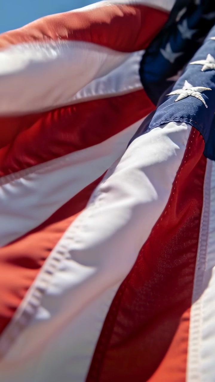 Vertical video: Rippling United States flag in midday breeze, low camera tracking stitched stars
