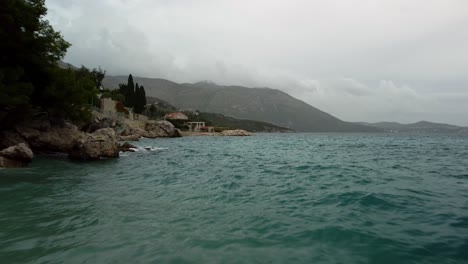 Un-Drone-Volando-Bajo-Disparado-Desde-La-Playa-A-Través-Del-Agua-Y-A-Lo-Largo-De-La-Costa-Rocosa-En-Línea-Y-Luego-Alrededor-Del-Puerto-De-Mlini,-Croacia