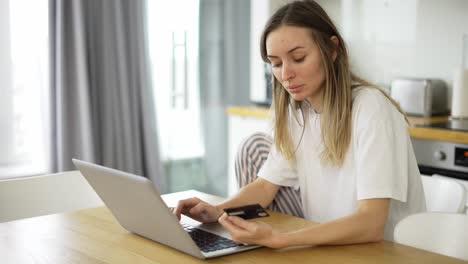 pretty girl is making online payment holding bank card using modern laptop at home