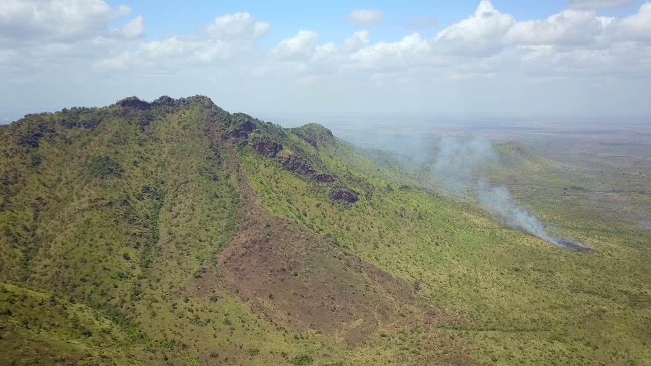 Smoke rising from slopes of mountain in Karamoja, Uganda, aerial view of wildfire burning dry vegetation, environmental damage, climate change, deforestation, global warming, pollution, disaster