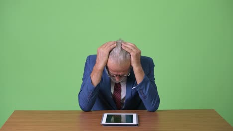 handsome senior bearded businessman against green background