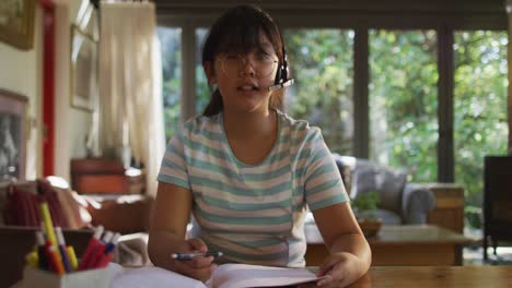 asian girl sitting at table wearing headphones and making video call