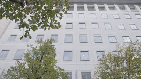people walk past the entrance of a modern office building surrounded by trees, tilt down shot