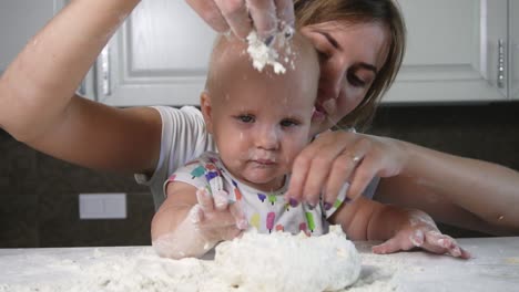 Young-mother-and-her-little-child-preparing-dough-and-pouring-flour-on-the-table.-Little-baby-playing-with-flour.-Family-girls