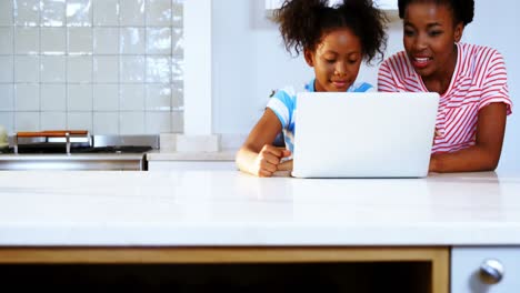 mother and daughter using laptop in kitchen