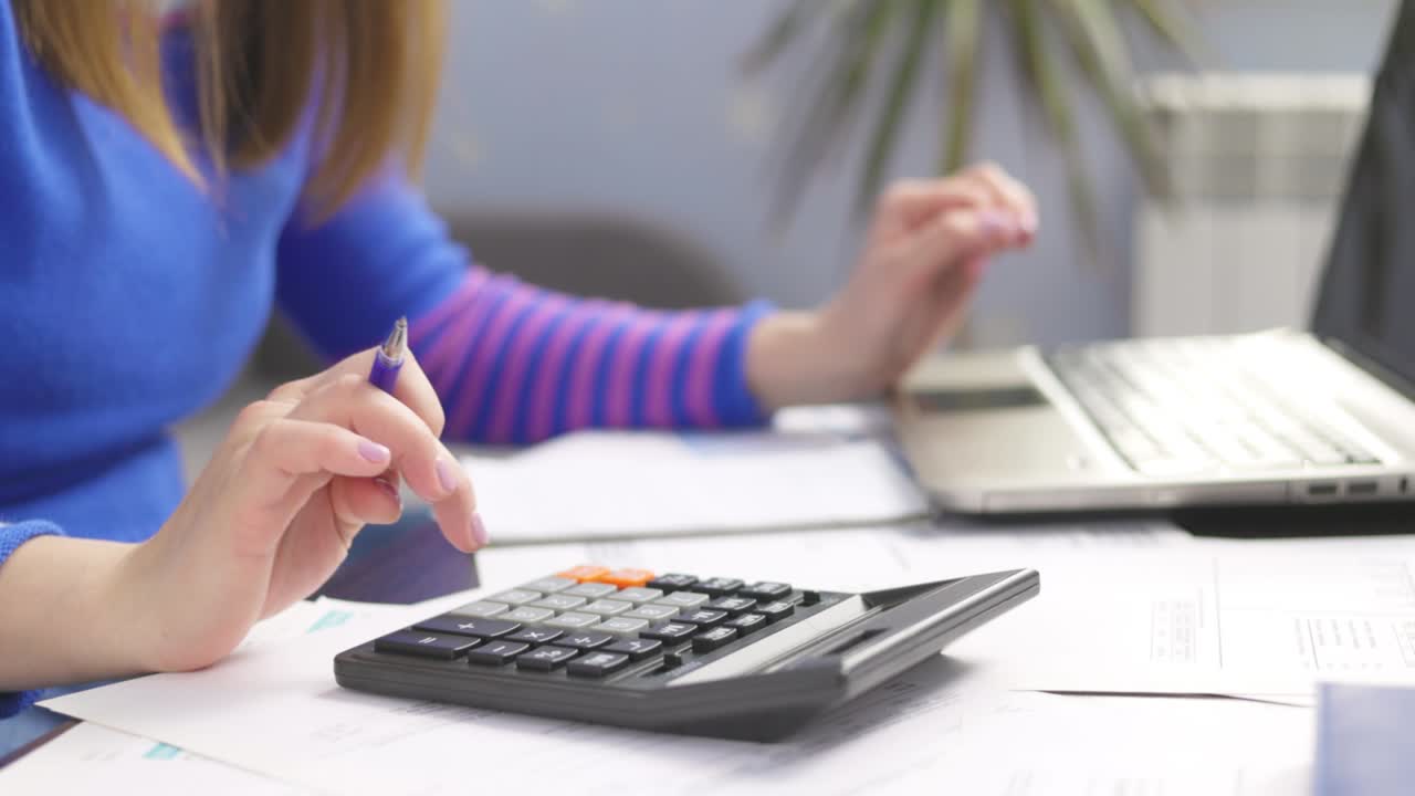 mujer usando calculadora para calcular facturas domésticas en el hogar, haciendo papeleo para pagar impuestos