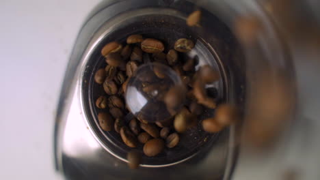 cámara lenta en una vista aérea cercana de granos de café frescos y marrones que se vierten en un elegante molinillo eléctrico para el café de la mañana