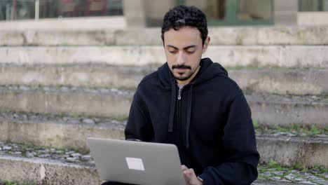 Un-Joven-Serio-Usando-Una-Computadora-Portátil-En-La-Calle