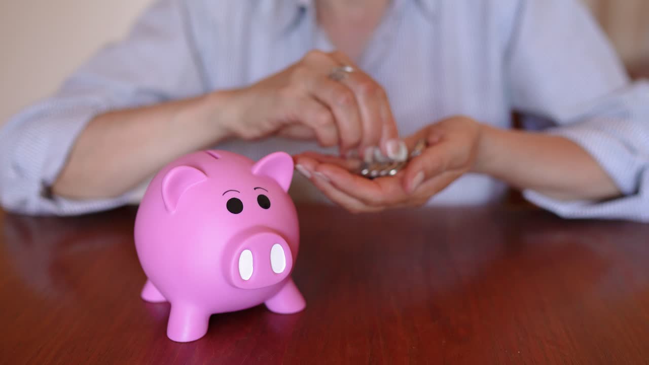 Woman's Hand Putting Coins On The Piggy Bank In The Wooden Table