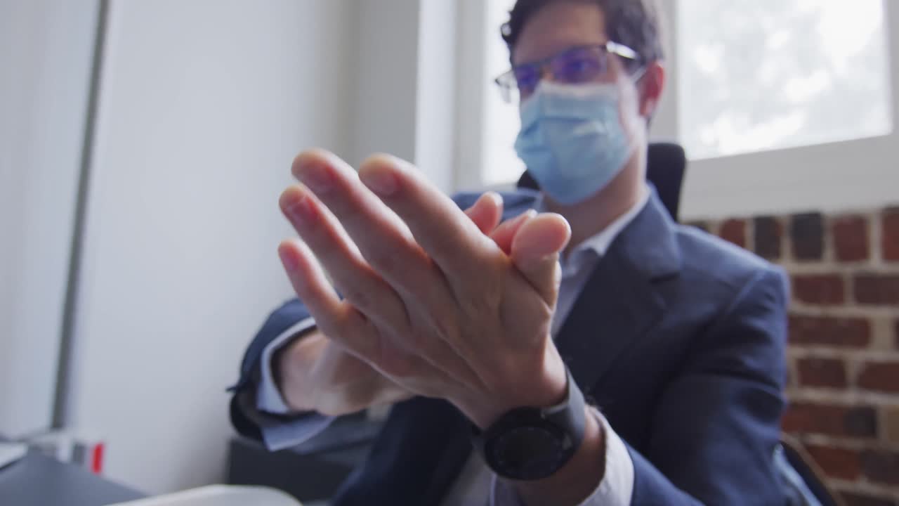 Uomo con mascherina che si disinfetta le mani in ufficio.