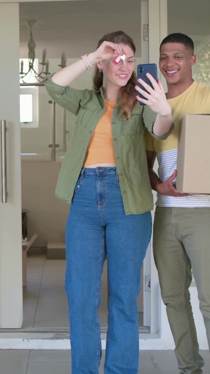 Video verticale: Donna in maglietta verde che registra, tenendo in mano telefono e telecomando sulla soglia, reagendo a una consegna