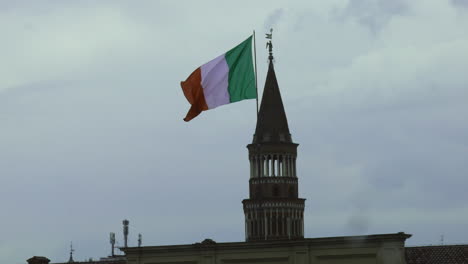 Large-Italian-Flag-on-a-cloudy-overcast-day,-with-a-church-in-the-background-in-Milan