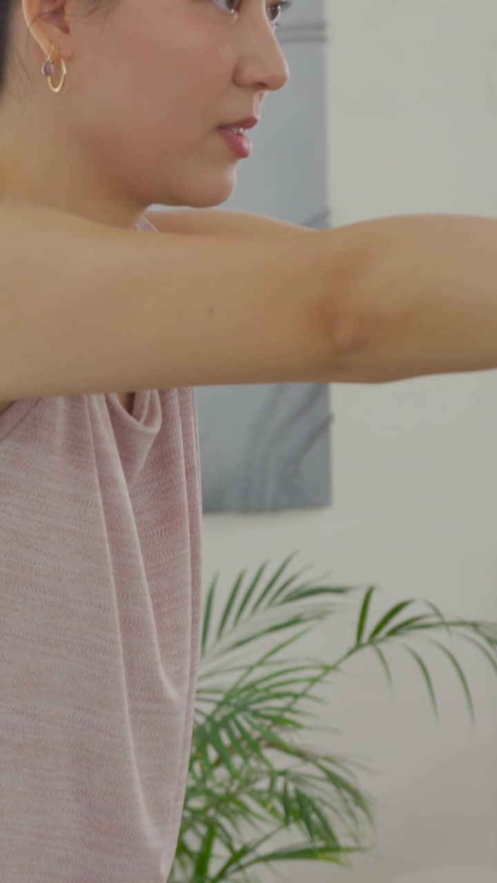 Video vertical: Cámara ascendiendo mostrando a una mujer con top rosa haciendo sentadillas, ejercitándose con una banda roja en casa.