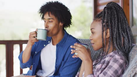 happy african american couple drinking coffee in log cabin, slow motion