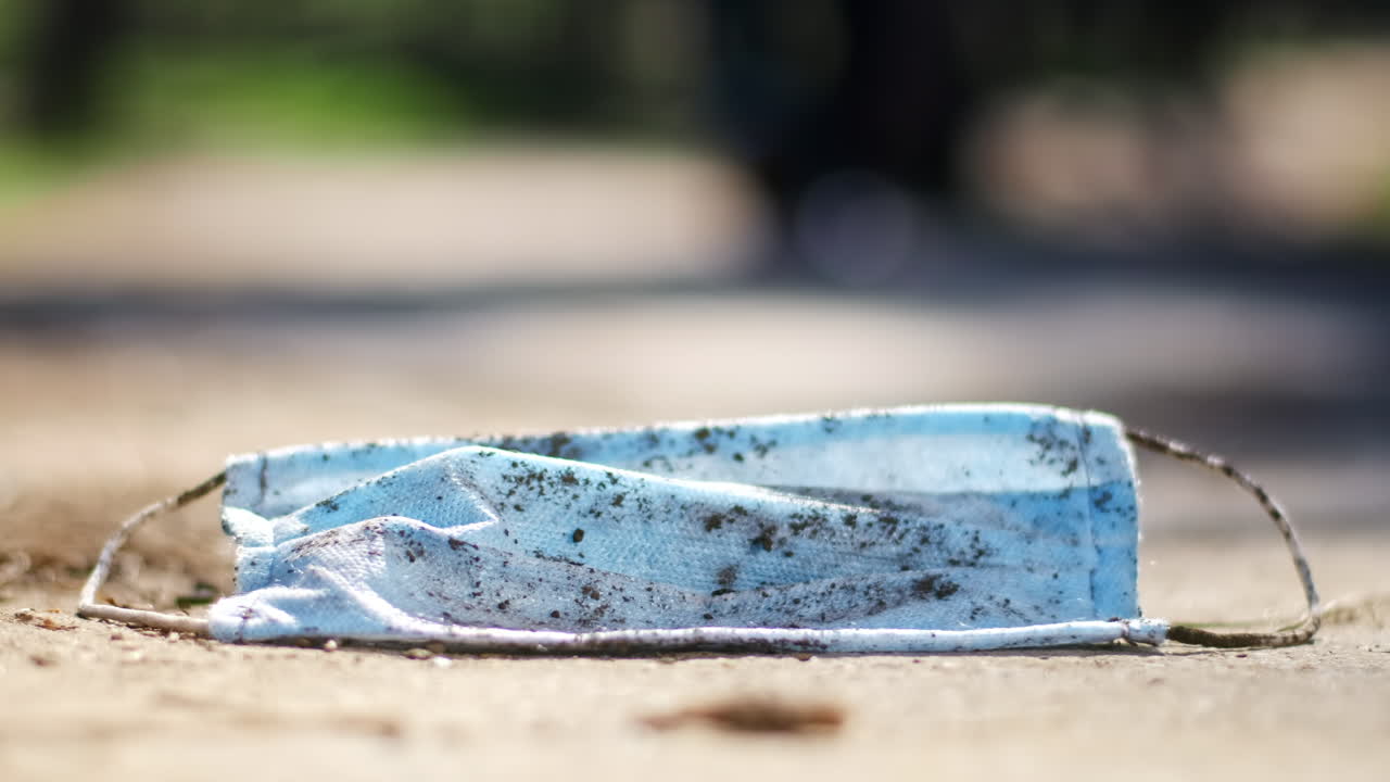 Man in medical gloves picking up dirty medical mask from the ground from the ground. Pollution idea