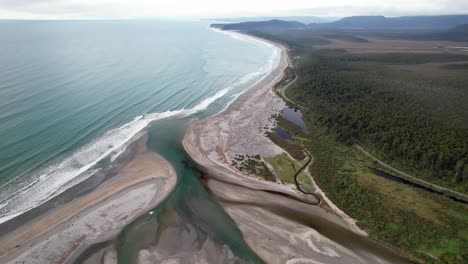 mahitahi river mouth on coastline of maori beach in bruce bay, new zealand. aerial pullback shot