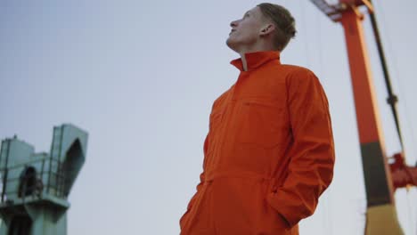 guapo joven trabajador de almacén de contenedores en uniforme naranja de pie junto al barco en el puerto