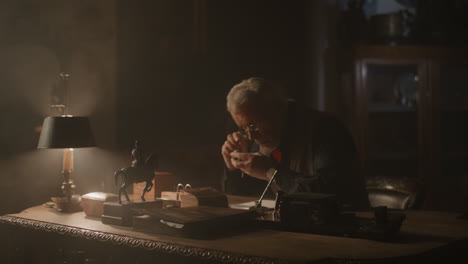 older passionate man evaluates an old silver skull watch in his office at night