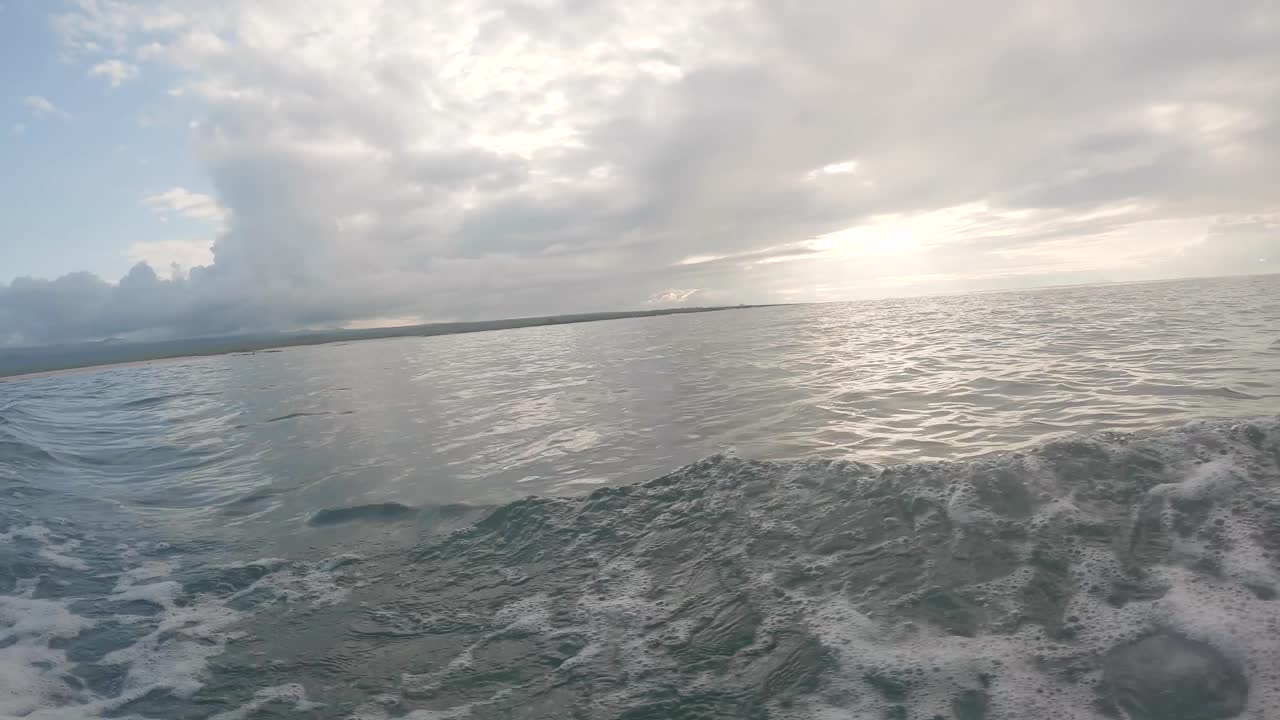The sun is being covered by white clouds on an island of the Galapagos islands. Waves are formed due to the movement of a boat