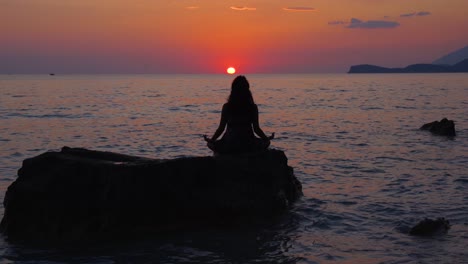 girl concentrated on yoga exercises stays frozen on cliff with sea view in front of sunset with colorful sky