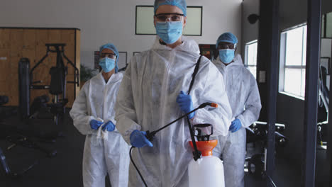 team of health workers wearing protective clothes holding disinfectant sprayer in the gym