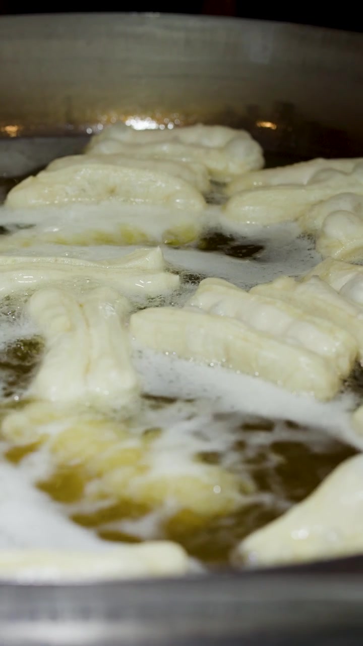 Close-up shot of dough sticks frying in bubbling oil within a large metal wok.