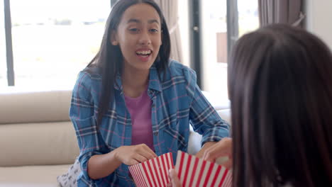 teenage girls eating popcorn and talking while hanging out at home