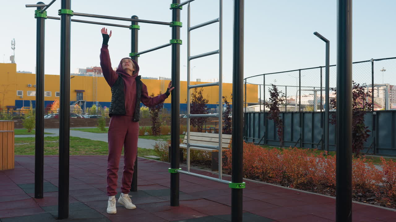 Female trainer placing hands on horizontal bar in urban park outdoor gym space for pull up exercise demonstrating balance and strength before dynamic workout with people moving in background