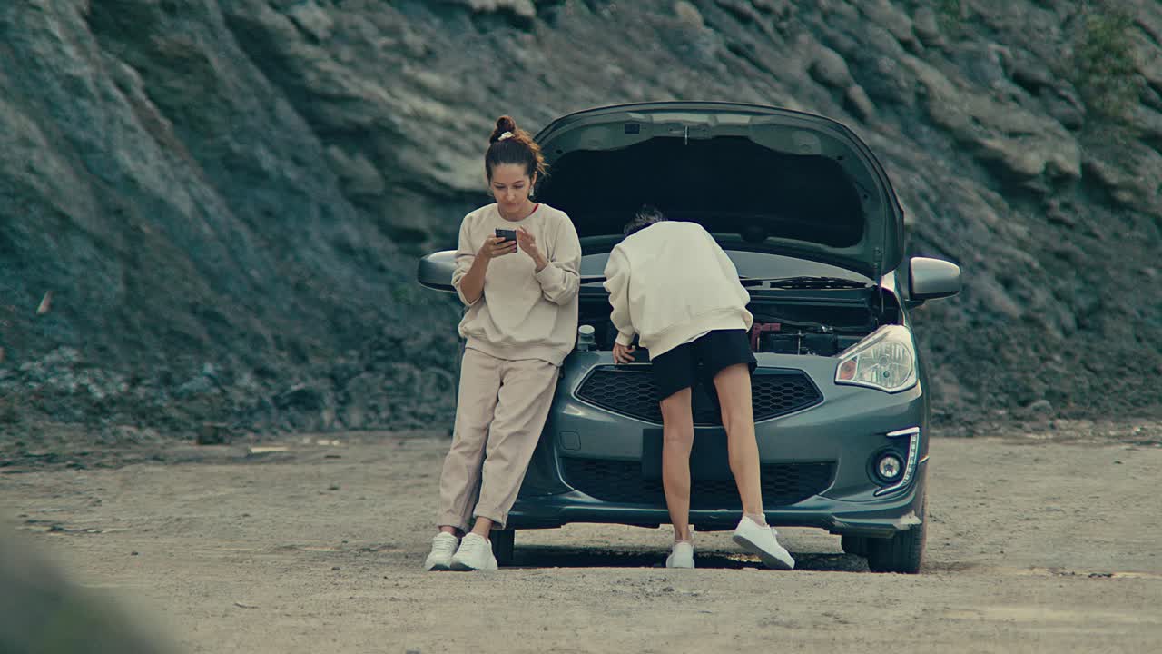 Two women dealing with a broken-down car in a desolate landscape