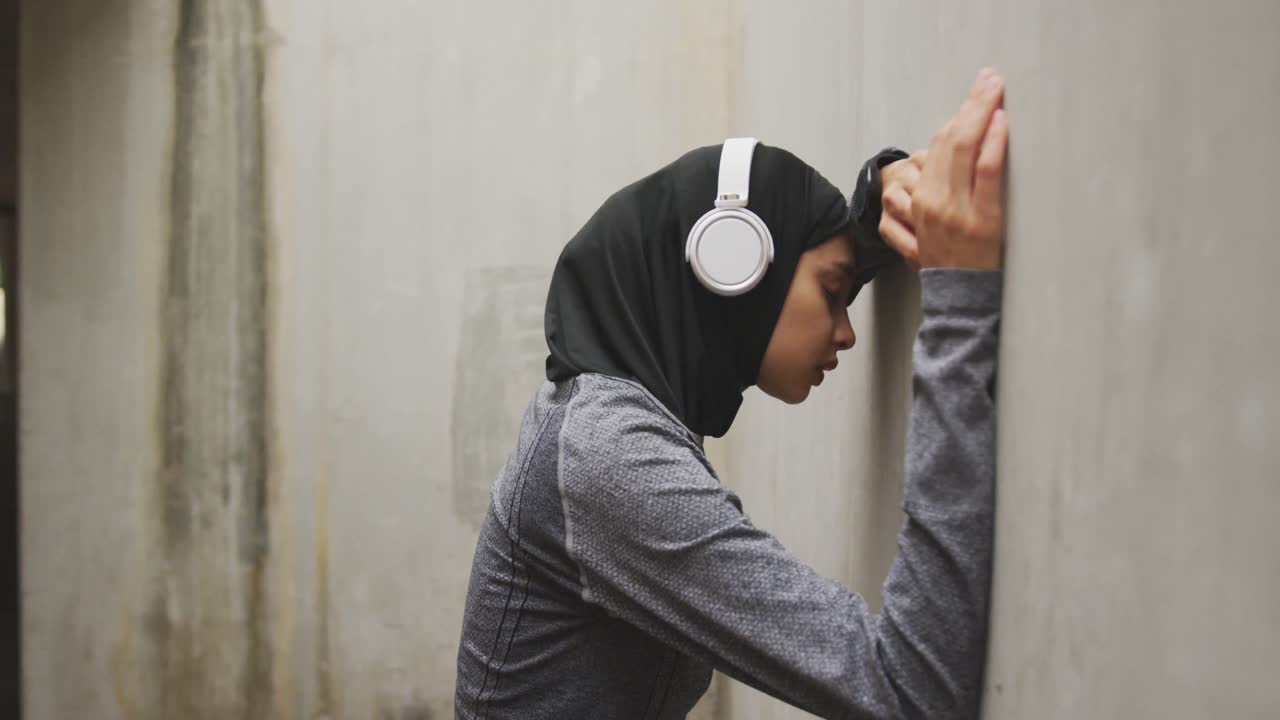 Exhausted woman in sportswear with wireless headphones wearing hijab
