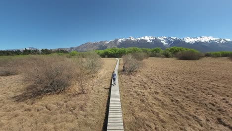 woman hiking on wooden boardwalk at glenorchy with distant new zealand mountains