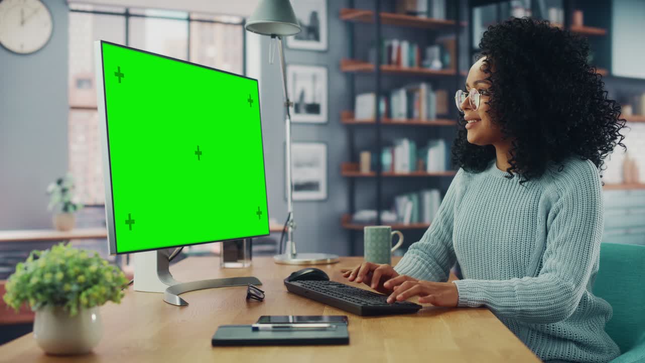 latina donna specialista che lavora su un computer desktop con schermo verde mock up display a casa salotto mentre è seduto a un tavolo. freelancer donna chiacchierare su internet sui social network.