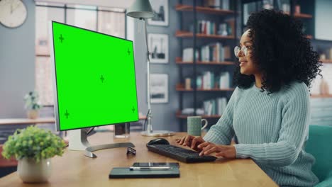 especialista latina que trabaja en una computadora de escritorio con pantalla verde en la sala de estar de su casa mientras está sentada en una mesa. mujer freelance hablando por internet en redes sociales.