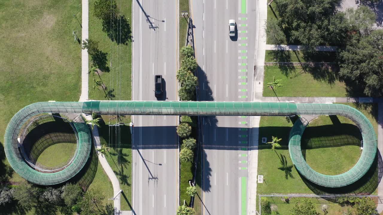 una vista aérea directamente sobre una pasarela peatonal que cruza una autopista de seis carriles en un día soleado en florida