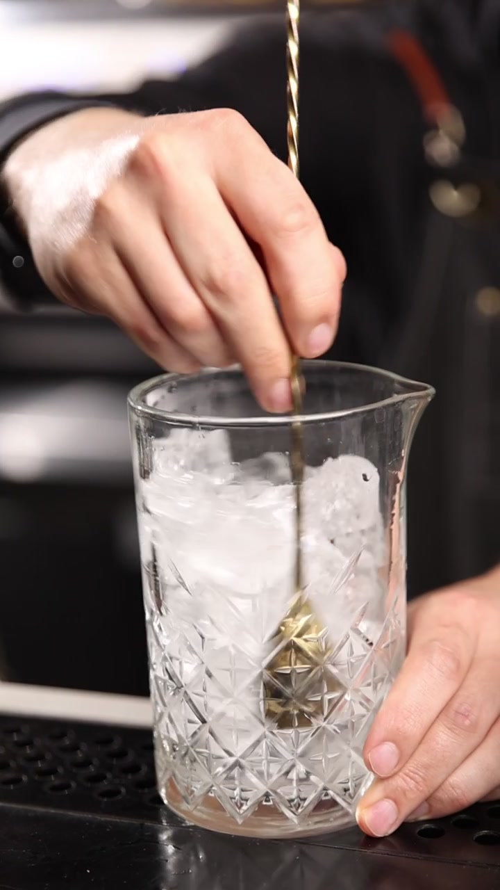 Barman professionista che mescola ghiaccio con un cucchiaio da bar in un mixing glass