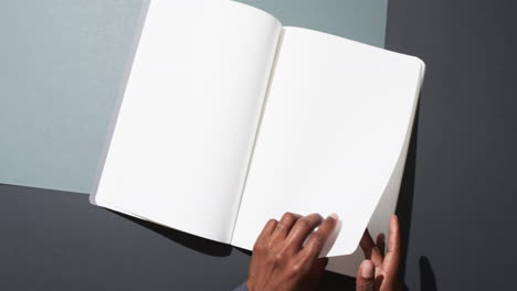 Video-of-hand-of-african-american-man-holding-book-with-blank-pages,-copy-space-on-black-background