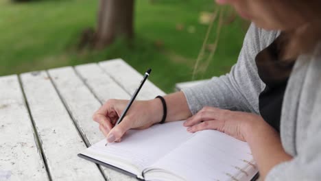 young caucasian women sitting in a lush green garden writing in her diary, slow push in