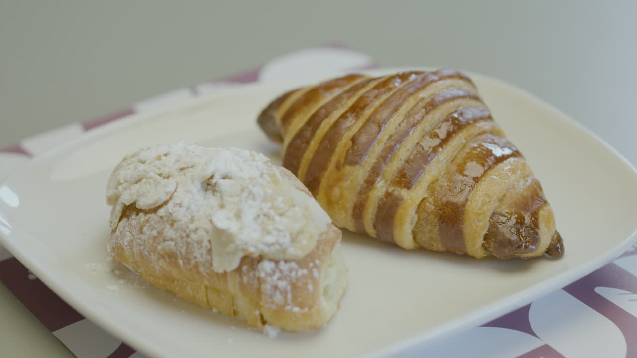 Close-up of two pieces of fresh pastry on a white plate: one glazed croissant and another covered with icing sugar