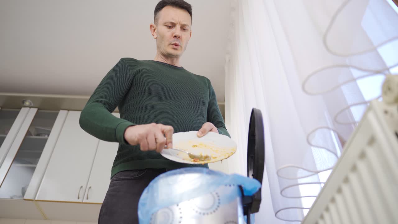Un uomo getta il cibo non mangiato da un piatto nella spazzatura