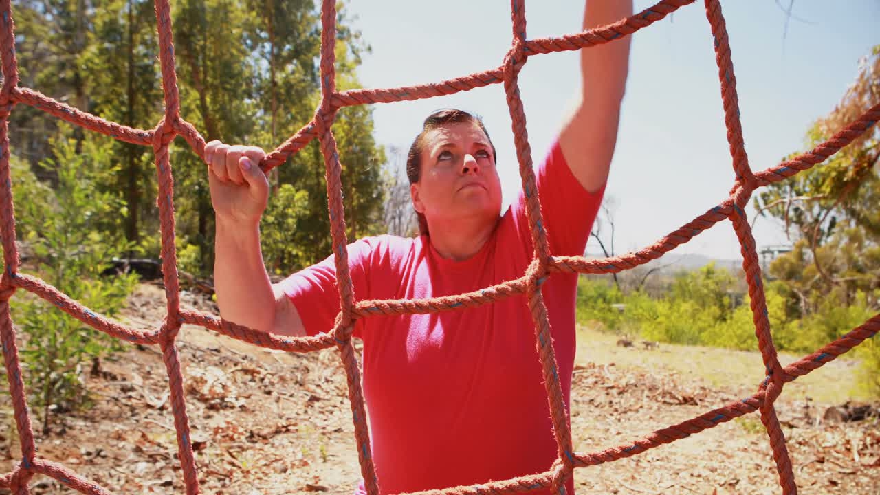 Determined woman climbing a net during obstacle course