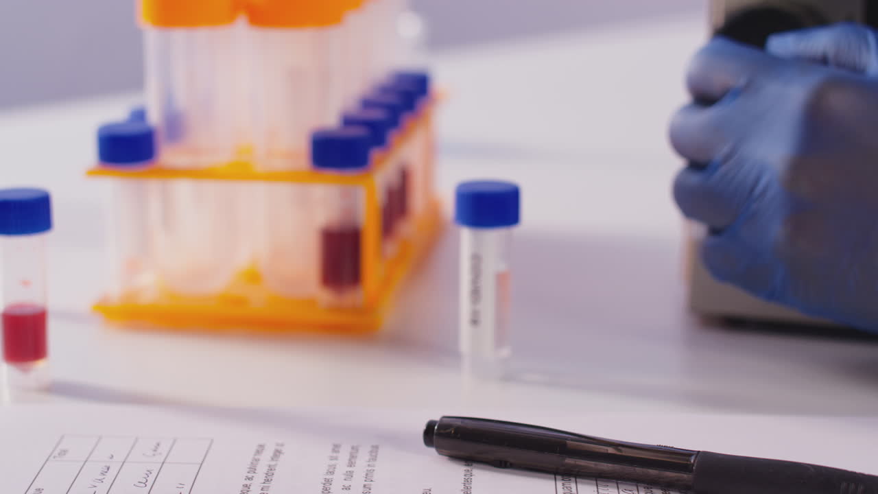 Close Up Of Female Lab Worker With Microscope Studying Test Tube Labelled Covid-19