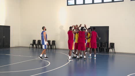 multiracial male basketball players celebrating, clapping hands and huddling in gym
