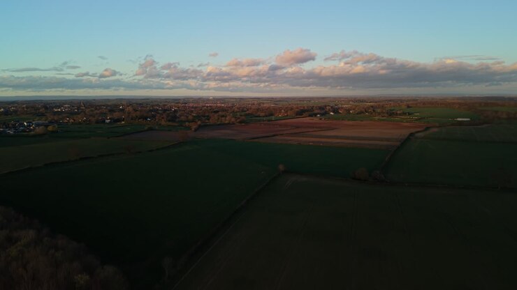 Aerial few of green farmers fields in North Yorkshire town at sunset with orange glow and shadows crossing the large flat fields