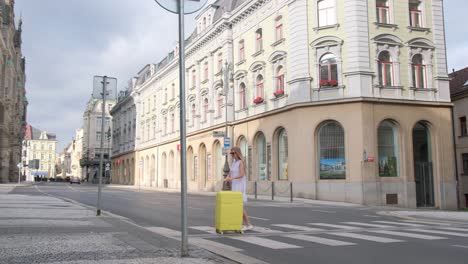 vertical video woman walking on the cobblestones against the background of the city, pulling a yellow suitcase. tourist woman travels. baggage. yellow suitcase