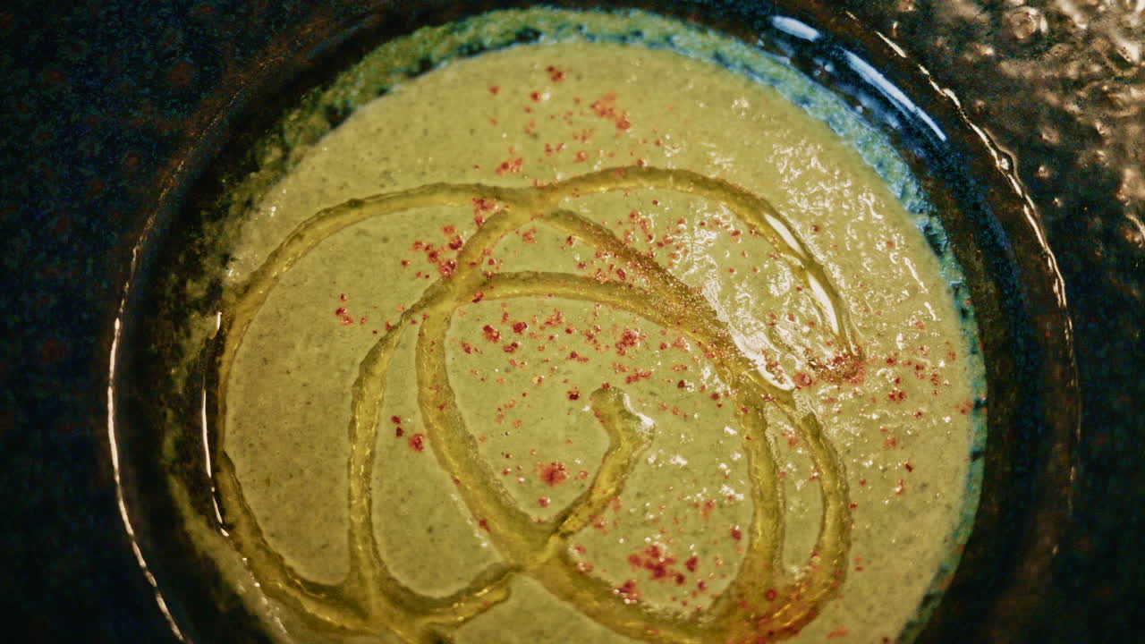 Vista superior de uma sopa verde cremosa decorada com óleo e especiarias, servida em uma tigela de cerâmica sobre uma mesa de madeira
