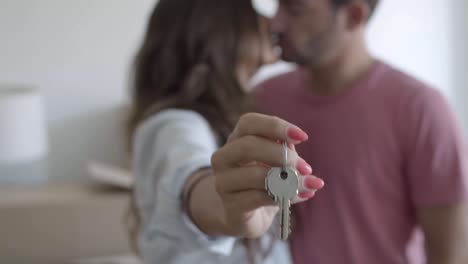 unfocused happy woman holding keys from new apartment, showing them at the camera and kissing boyfriend