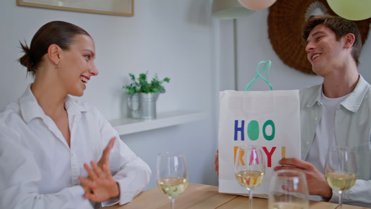 Smiling girl giving present to friend at birthday closeup. Guy opening package