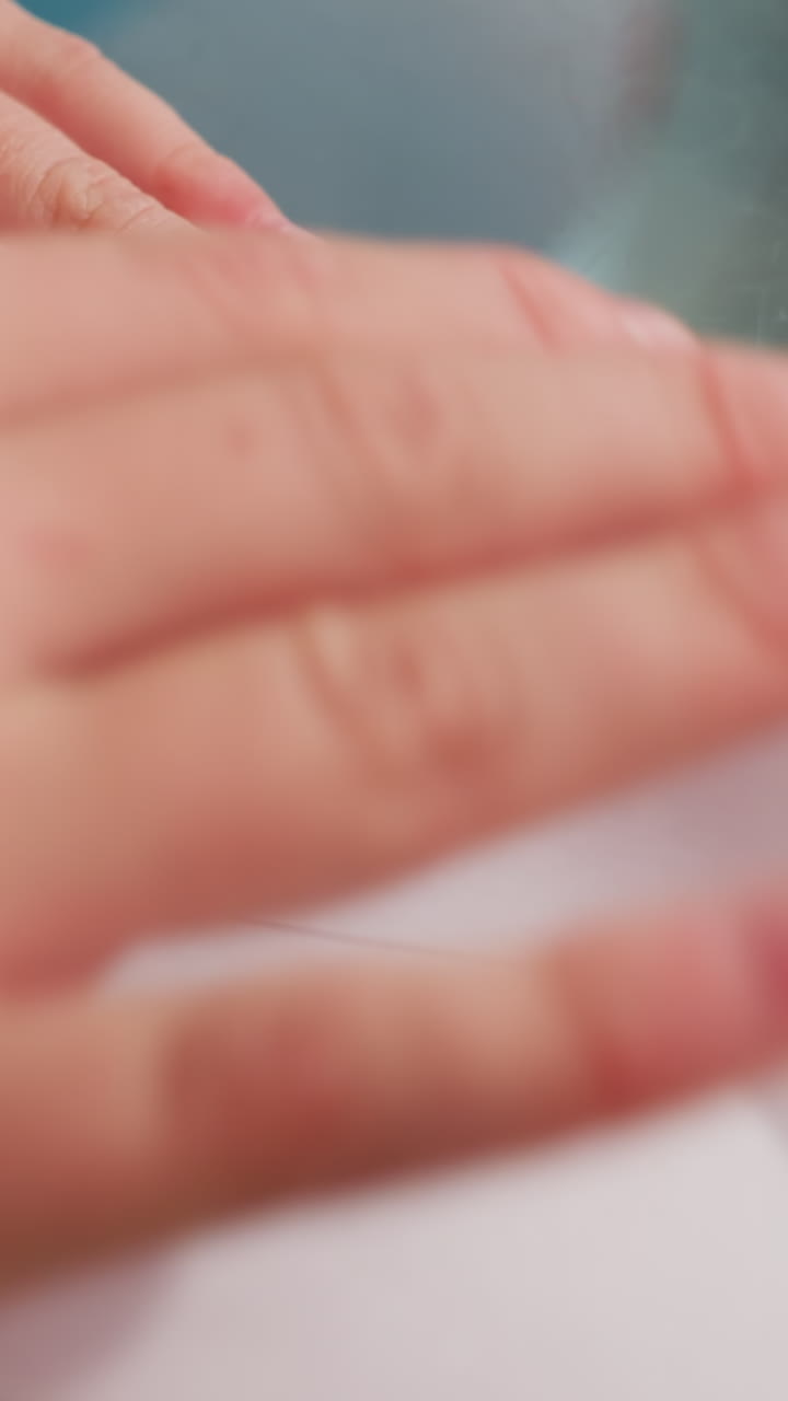 Child shapes paper, Child carefully folds paper for flight, Young child gently presses final fold on airplane, Child smiles softly as delicate paper airplane takes shape on glass surface