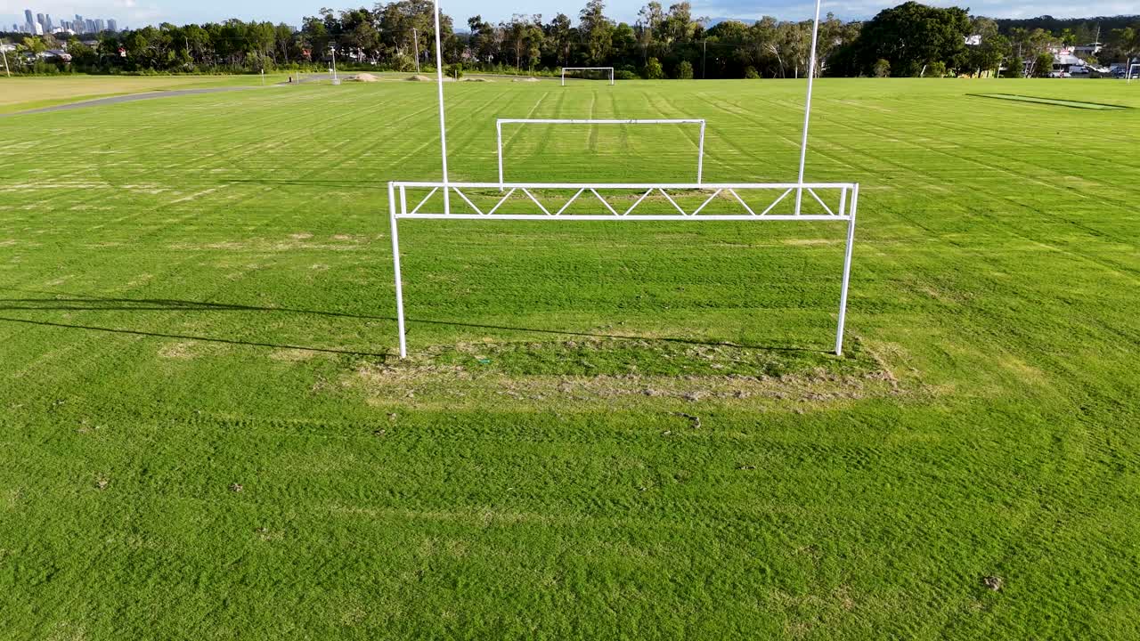 Drone footage captures a lush green soccer field with goalposts under clear skies, showcasing the expansive sports facility